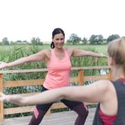 Zwei Frauen praktizieren Sport auf einer Holzterrasse, umgeben von Natur, als Teil ihrer Sporttherapie.